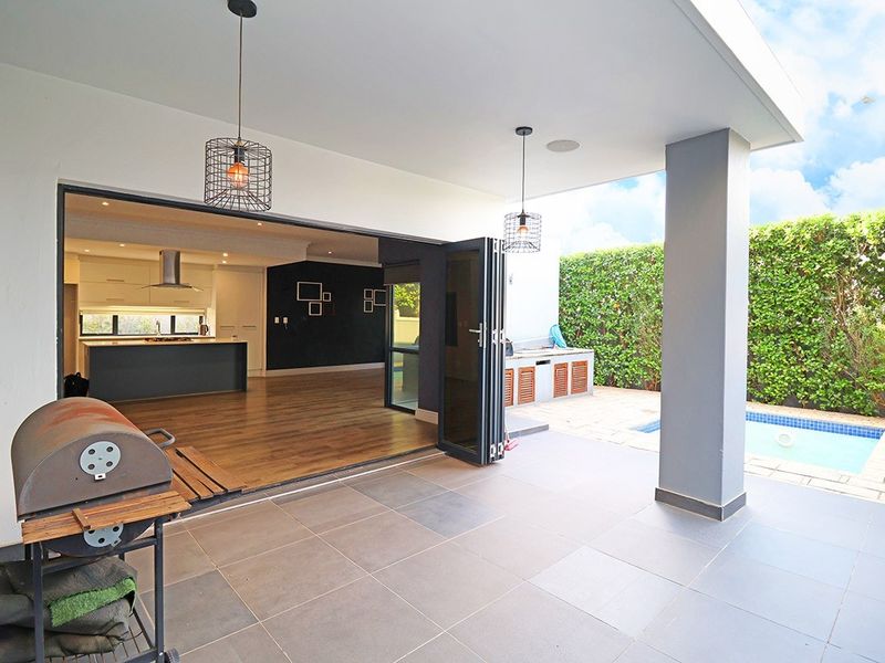 Covered patio area featuring large bi-fold doors opening to an open-plan interior, built-in braai, and direct access to a swimming pool and garden.