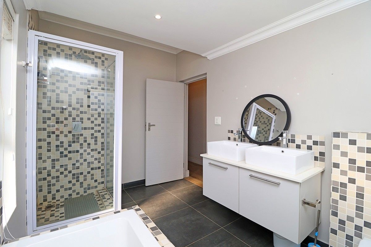Modern bathroom featuring a double vanity with vessel sinks, a glass-enclosed shower with mosaic tiling, and neutral wall finishes.