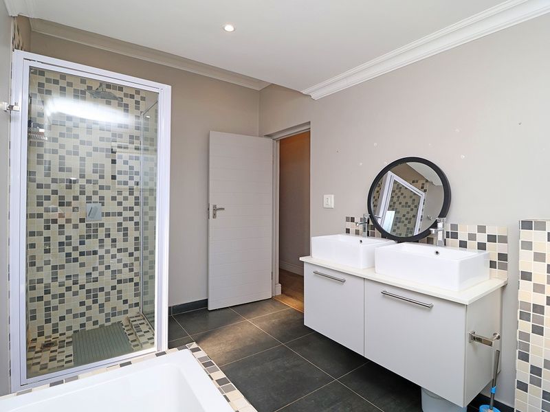 Modern bathroom featuring a double vanity with vessel sinks, a glass-enclosed shower with mosaic tiling, and neutral wall finishes.