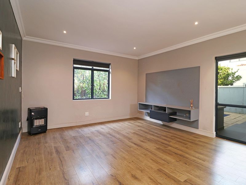 A bright and spacious living room featuring modern laminate flooring, recessed downlights, and a built-in media console with direct access to the outdoor area.