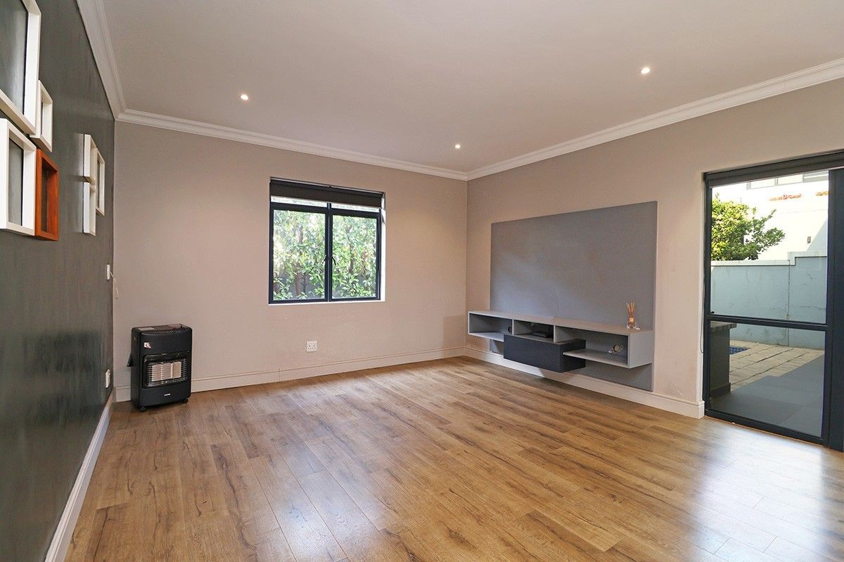 A bright and spacious living room featuring modern laminate flooring, recessed downlights, and a built-in media console with direct access to the outdoor area.