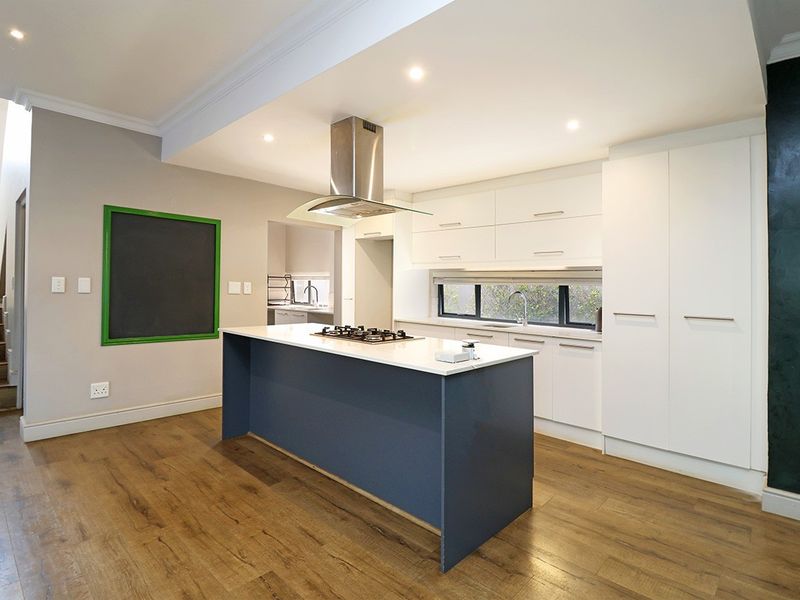 Modern kitchen featuring a central island with a gas hob, sleek white cabinetry, and high-quality laminate flooring, with an adjacent scullery area.