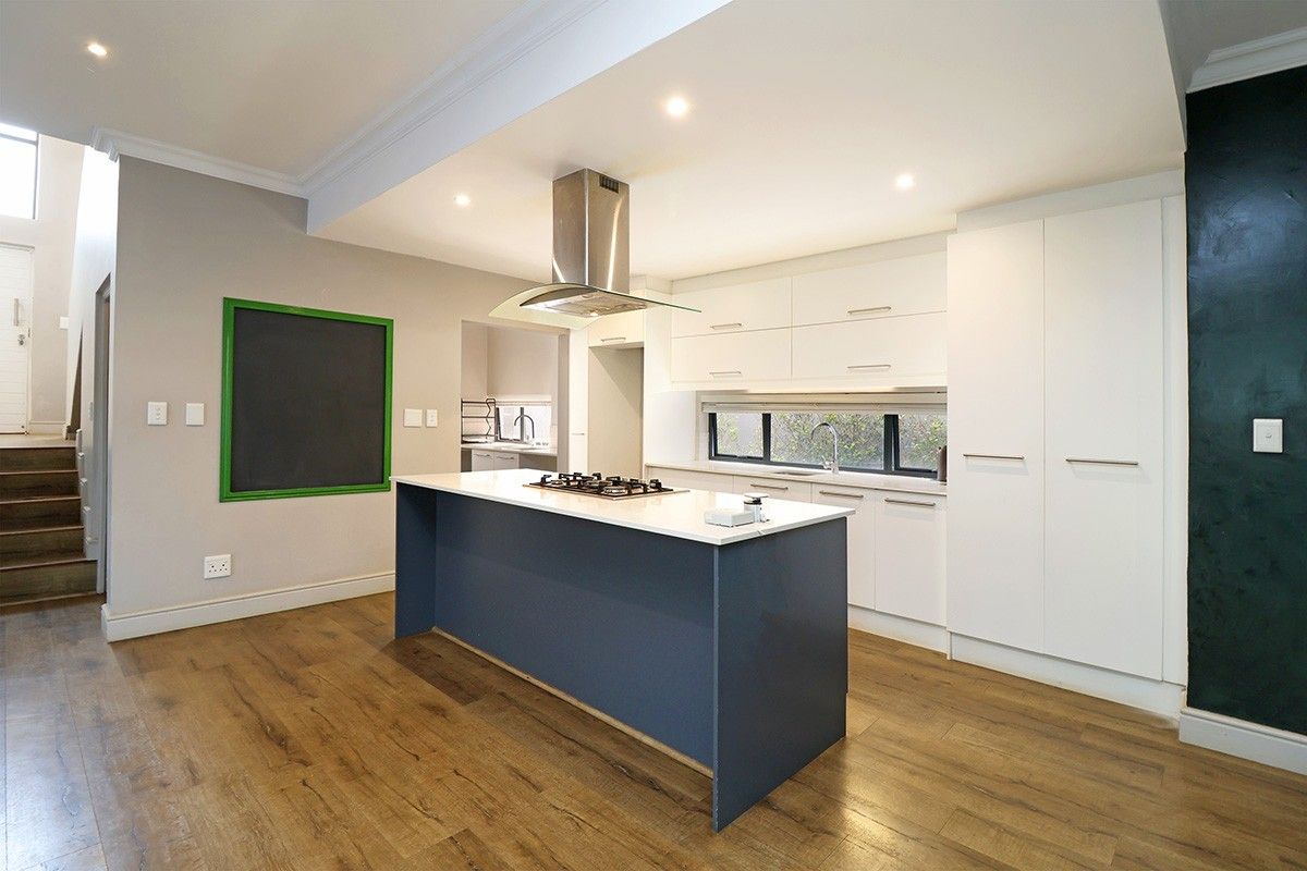 Modern kitchen featuring a central island with a gas hob, sleek white cabinetry, and high-quality laminate flooring, with an adjacent scullery area.