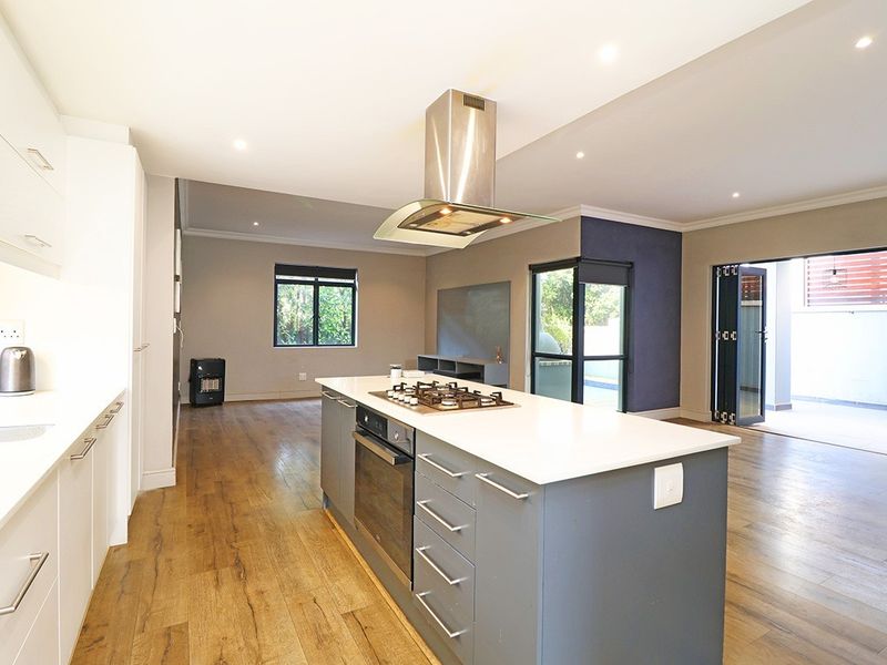 Spacious open-plan kitchen and living area featuring a central island with gas hob, modern cabinetry, and seamless flow to the outdoor patio through bi-fold doors.