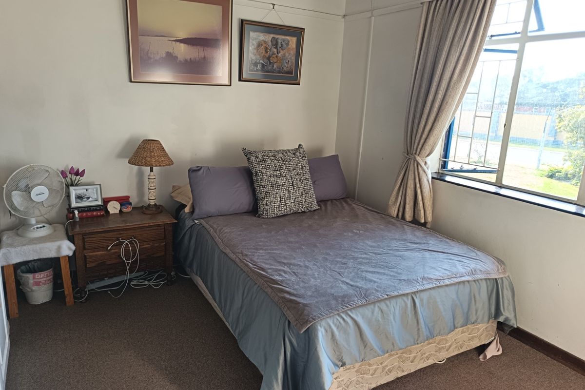 A functional bedroom featuring carpeted flooring and a large window with curtain rails, providing natural light and a view of the exterior.
