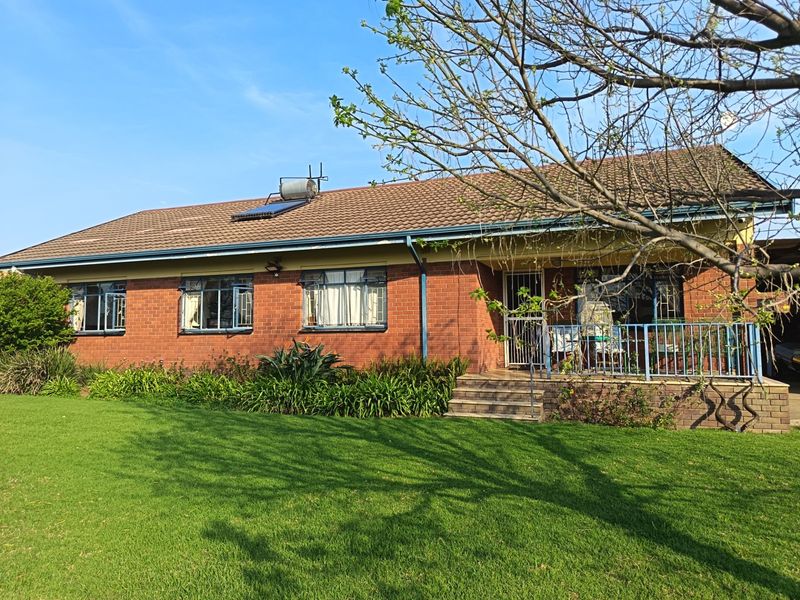 Rear view of a single-story brick house featuring a tiled roof, solar water heater, and a raised patio area with metal railings.
