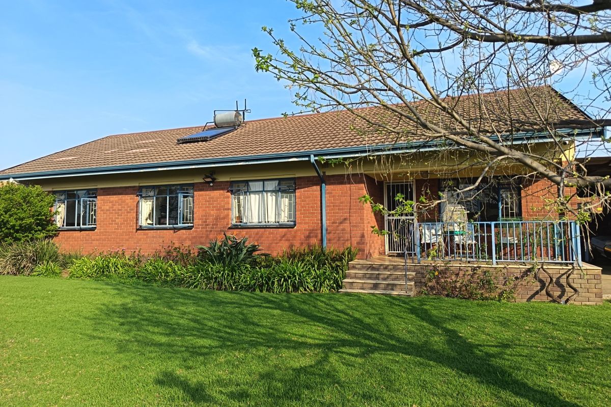 Rear view of a single-story brick house featuring a tiled roof, solar water heater, and a raised patio area with metal railings.