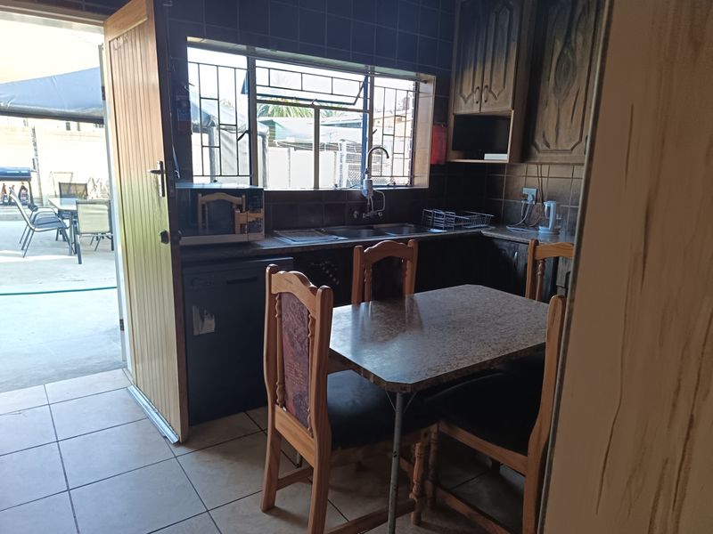 A functional kitchen featuring built-in cabinetry, tiled splashbacks, and a double sink, with direct access to an outdoor patio area.