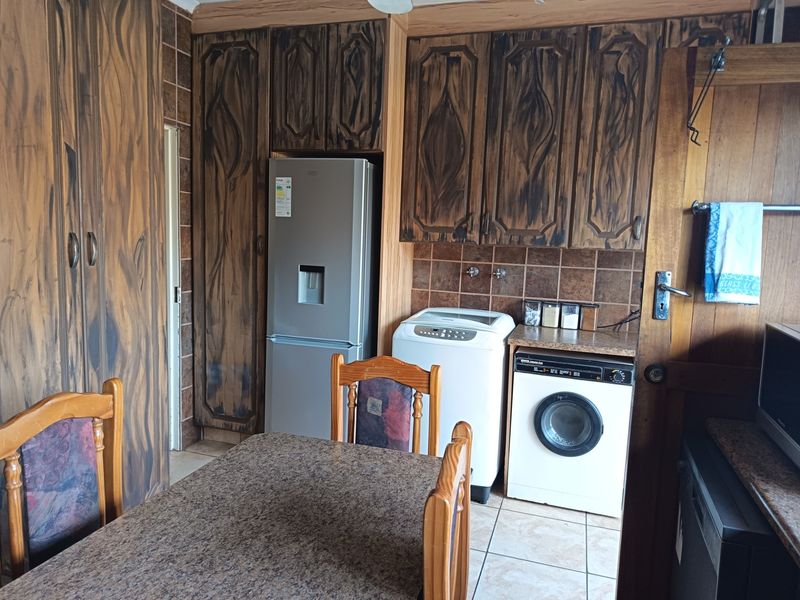A functional kitchen area featuring built-in cabinetry, tiled backsplash, and integrated laundry appliances, offering potential for modernization and aesthetic updates.