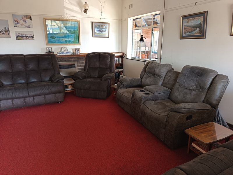 A living room featuring a brick fireplace, built-in shelving, and casement windows, currently finished with red carpeting.
