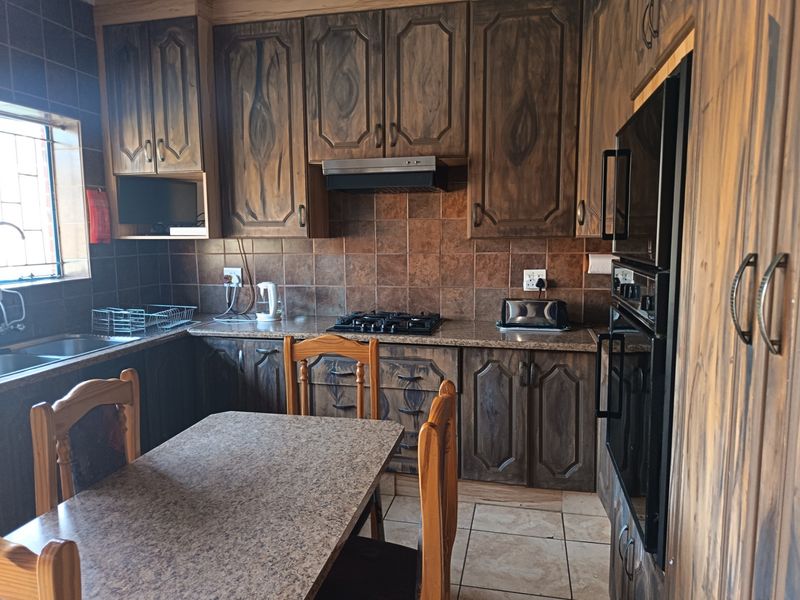 A functional kitchen featuring dark wood cabinetry, granite countertops, a gas hob, extractor fan, and built-in oven with tiled backsplash and flooring.