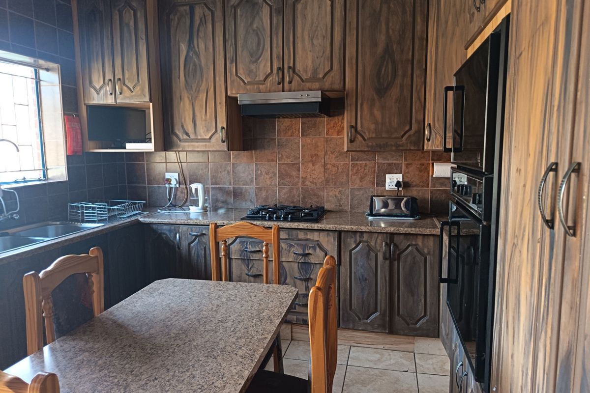 A functional kitchen featuring dark wood cabinetry, granite countertops, a gas hob, extractor fan, and built-in oven with tiled backsplash and flooring.