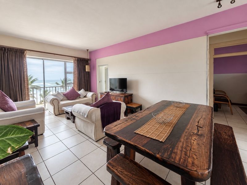 Open-plan living and dining area featuring ceramic floor tiles and large sliding glass doors providing direct access to a balcony with ocean views.