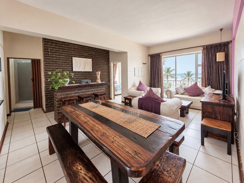 Spacious open-plan living and dining area featuring a brick accent wall, tiled floors, and large sliding doors opening to a balcony with ocean views.