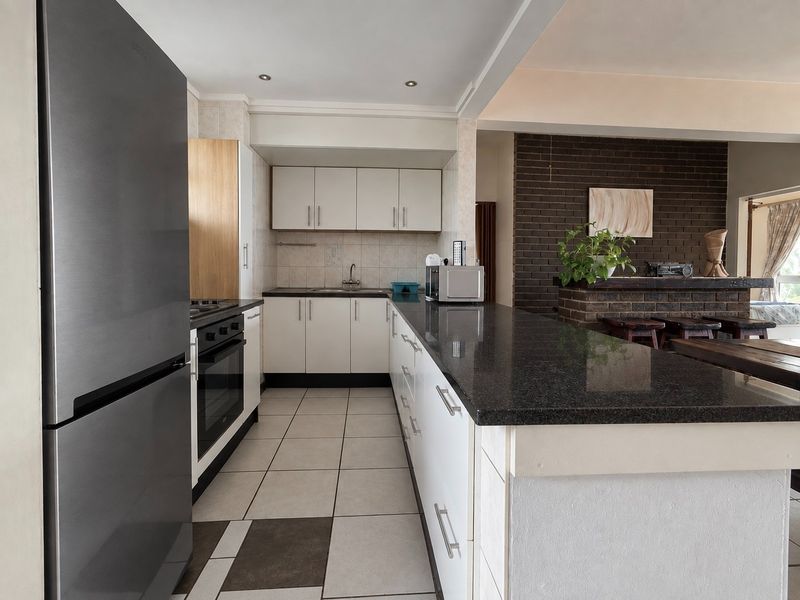 Open-plan kitchen featuring granite countertops, built-in cabinetry, and a breakfast bar, seamlessly flowing into a living area with an exposed brick feature wall.