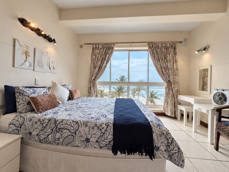 A bright bedroom featuring tiled flooring and a large sliding window offering scenic ocean views.