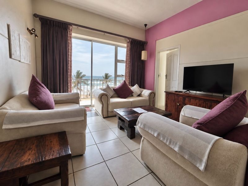 A comfortable living room featuring tiled floors and a large sliding glass door that opens onto a balcony with ocean views.