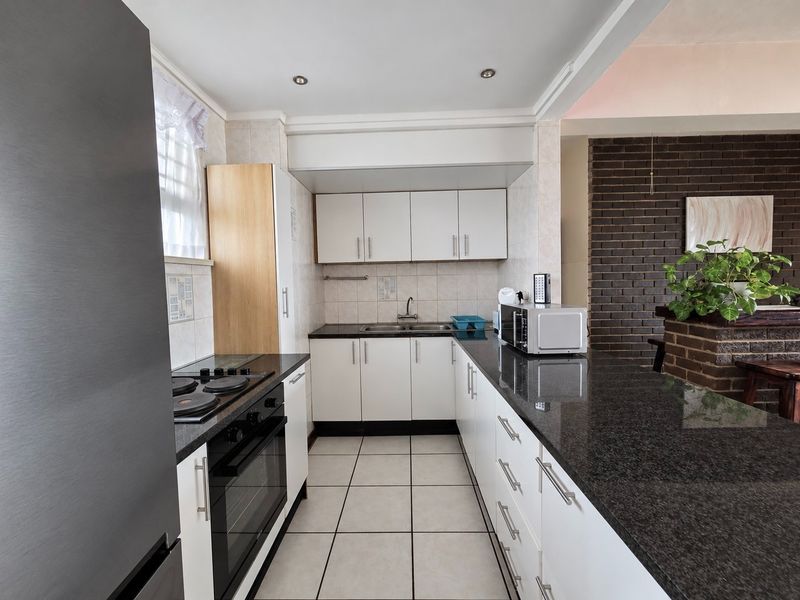 A functional kitchen featuring white cabinetry, dark granite countertops, tiled flooring, and integrated appliances, with an open-plan layout connecting to the living area.