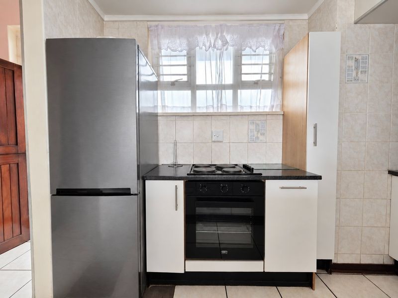 Compact kitchen featuring a built-in oven, electric hob, stone countertops, and tiled backsplash with neutral cabinetry.