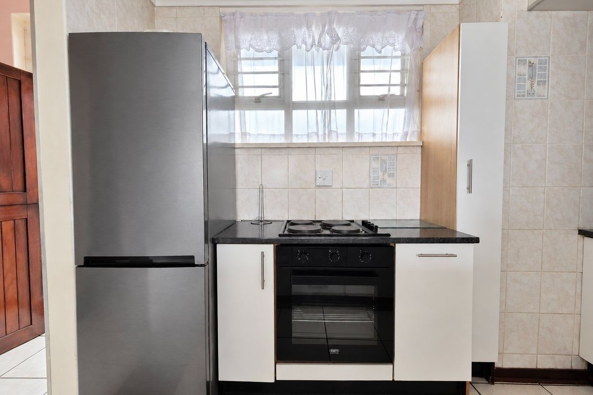 Compact kitchen featuring a built-in oven, electric hob, stone countertops, and tiled backsplash with neutral cabinetry.