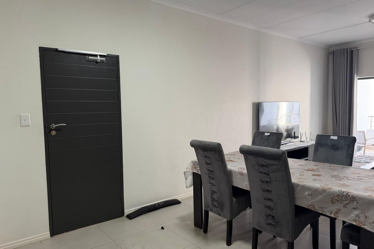 A living and dining area featuring tiled flooring and a dark-toned internal door, with neutral wall finishes and access to an adjacent outdoor space.