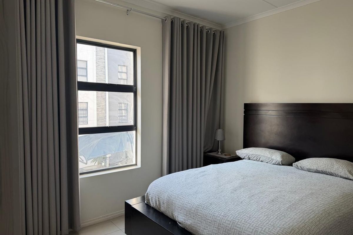 A well-maintained bedroom featuring neutral wall tones, tiled flooring, and a large window with fitted curtain tracks.