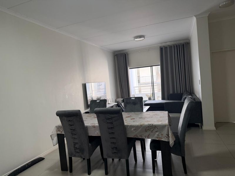 Open-plan living and dining area featuring neutral tiled flooring, coved ceilings, and a sliding glass door providing access to the balcony.