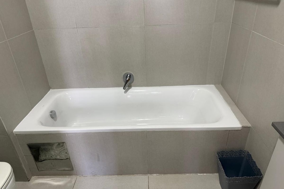 A clean bathroom featuring a built-in bathtub with wall-mounted fixtures and neutral floor-to-ceiling tiling.