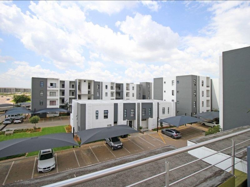 Elevated view overlooking a modern apartment complex with paved parking bays and shade cloth carports.