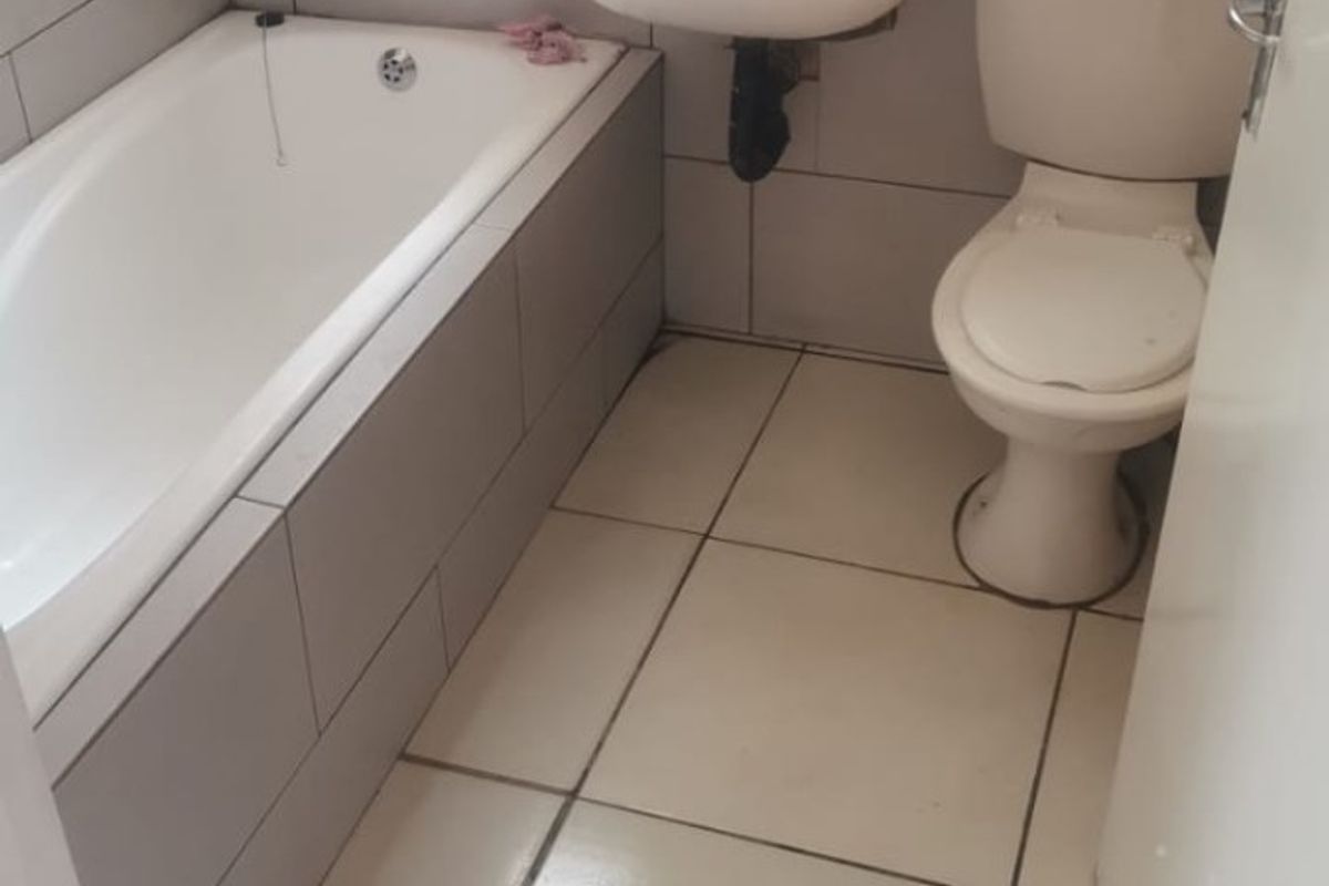 A compact bathroom featuring a built-in bathtub, wall-mounted basin, and toilet with neutral wall and floor tiling.