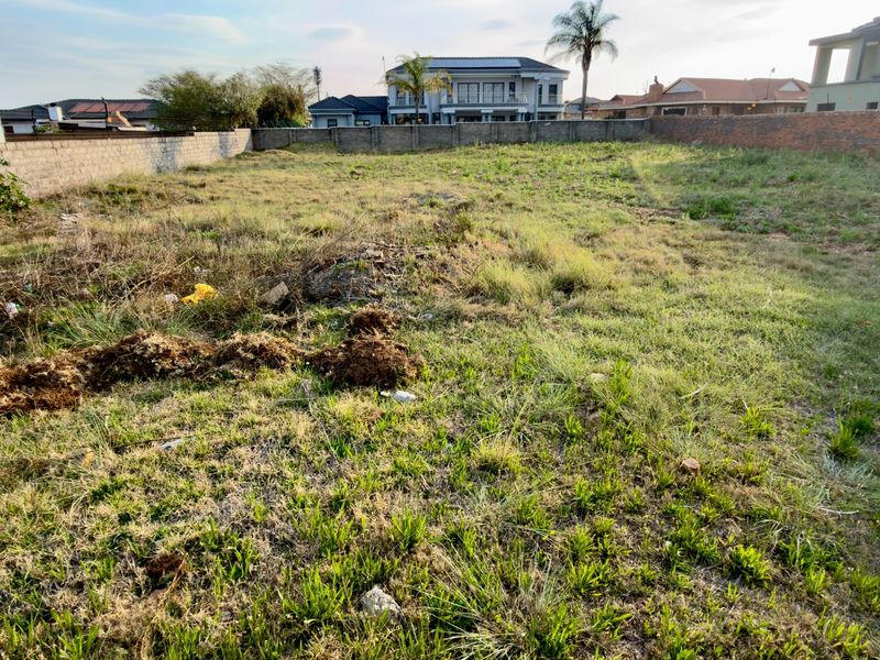A vacant residential plot featuring perimeter boundary walls and natural grass coverage, situated in an established neighborhood.