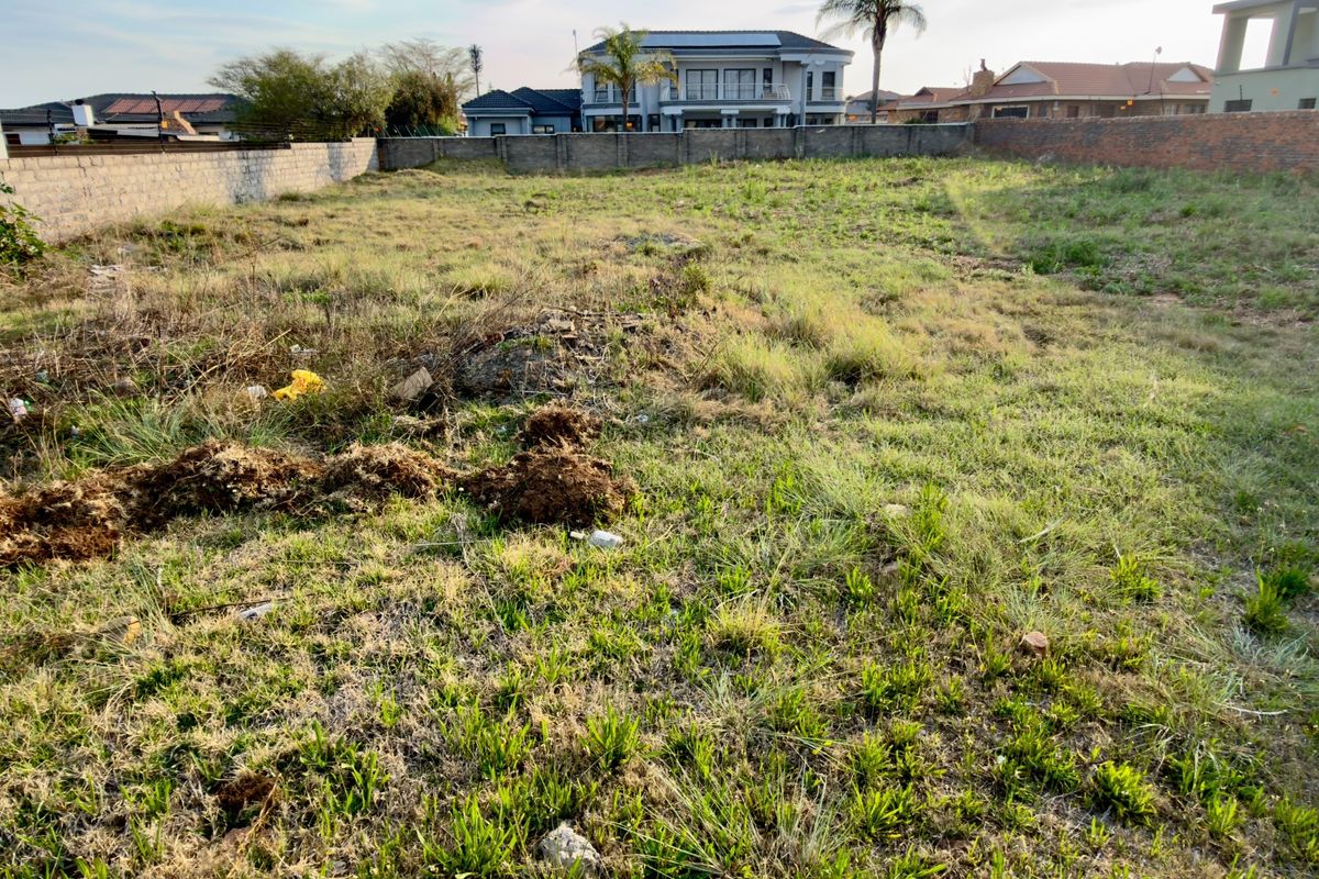 A vacant residential plot featuring perimeter boundary walls and natural grass coverage, situated in an established neighborhood.