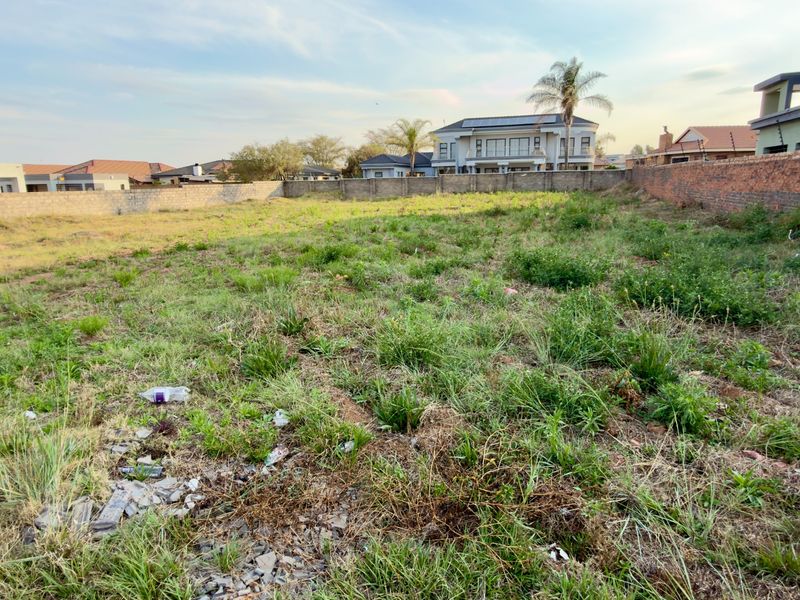 A vacant residential plot featuring perimeter boundary walls and natural grass cover, situated in an established neighborhood.