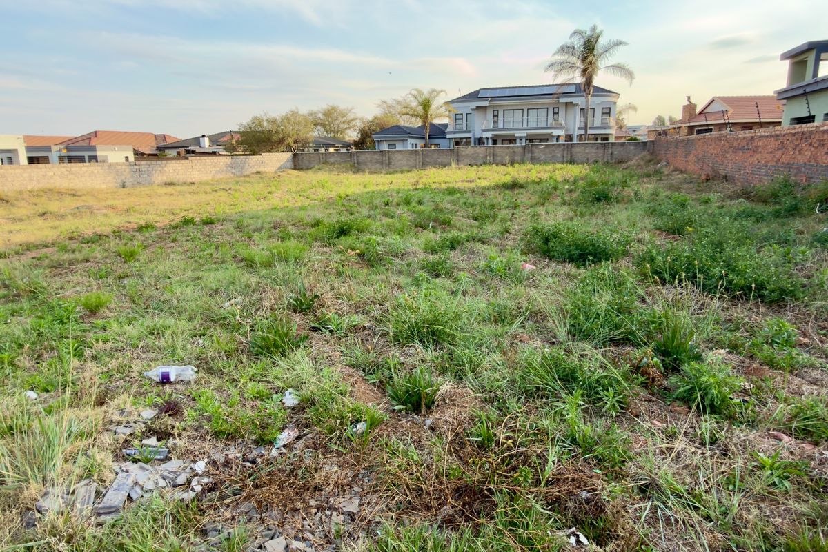 A vacant residential plot featuring perimeter boundary walls and natural grass cover, situated in an established neighborhood.