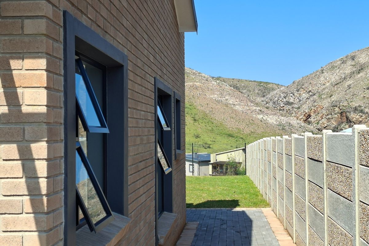 Side view of the property featuring face brick exterior, modern aluminium windows, a paved walkway, and a precast boundary wall with mountain views.