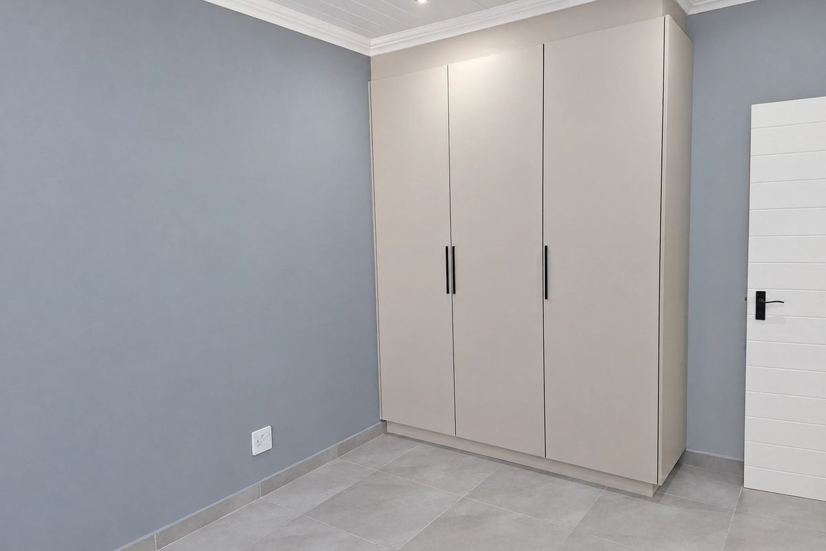 A clean, modern bedroom featuring neutral-toned built-in cupboards, grey tiled flooring, and crisp white ceiling finishes with recessed lighting.