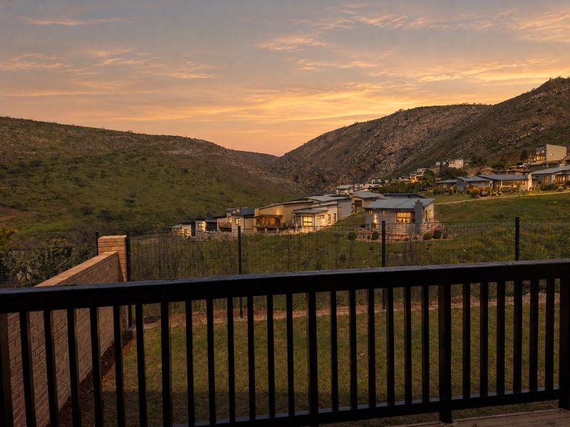 Scenic elevated view overlooking a residential estate nestled in a valley with mountain backdrop at sunset.