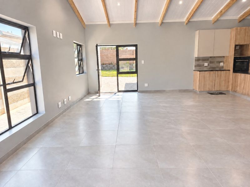 Spacious open-plan living area featuring modern tiled floors, exposed timber ceiling beams, and a contemporary kitchen with built-in cabinetry and oven.