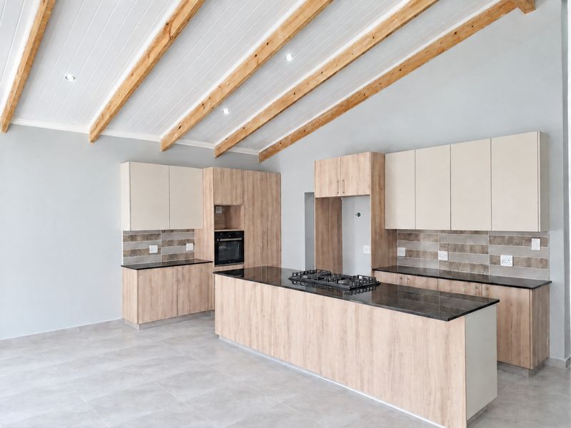 Modern kitchen featuring a large island with a gas hob, built-in oven, light wood cabinetry, tiled backsplash, and striking exposed timber ceiling beams.