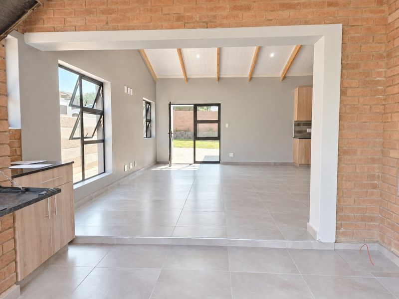 Spacious open-plan living area featuring exposed brick walls, timber ceiling beams, and large aluminium windows leading to the rear garden.