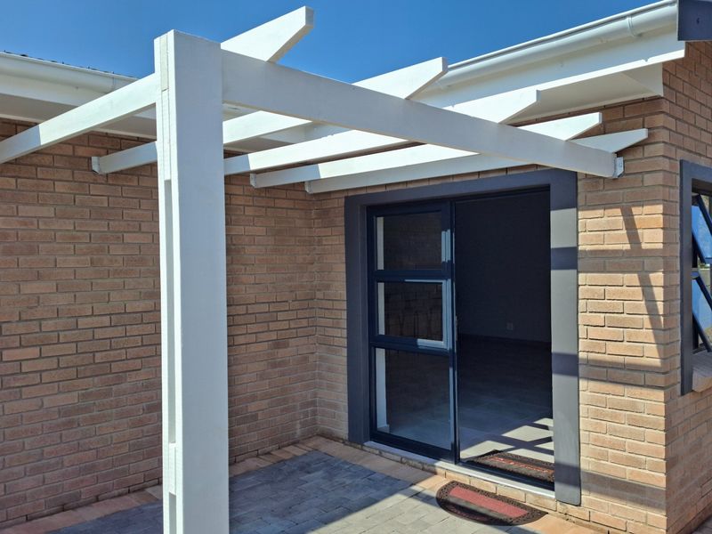 A neat outdoor patio area featuring a white timber pergola, brick exterior walls, and a modern sliding glass door leading into the home.
