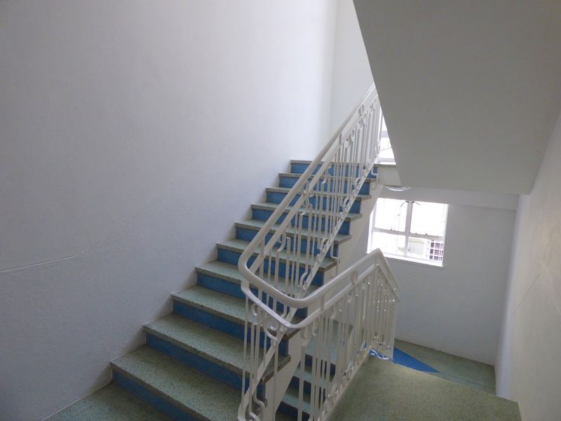 A functional commercial stairwell featuring terrazzo steps, a white metal balustrade, and natural light from a side window.