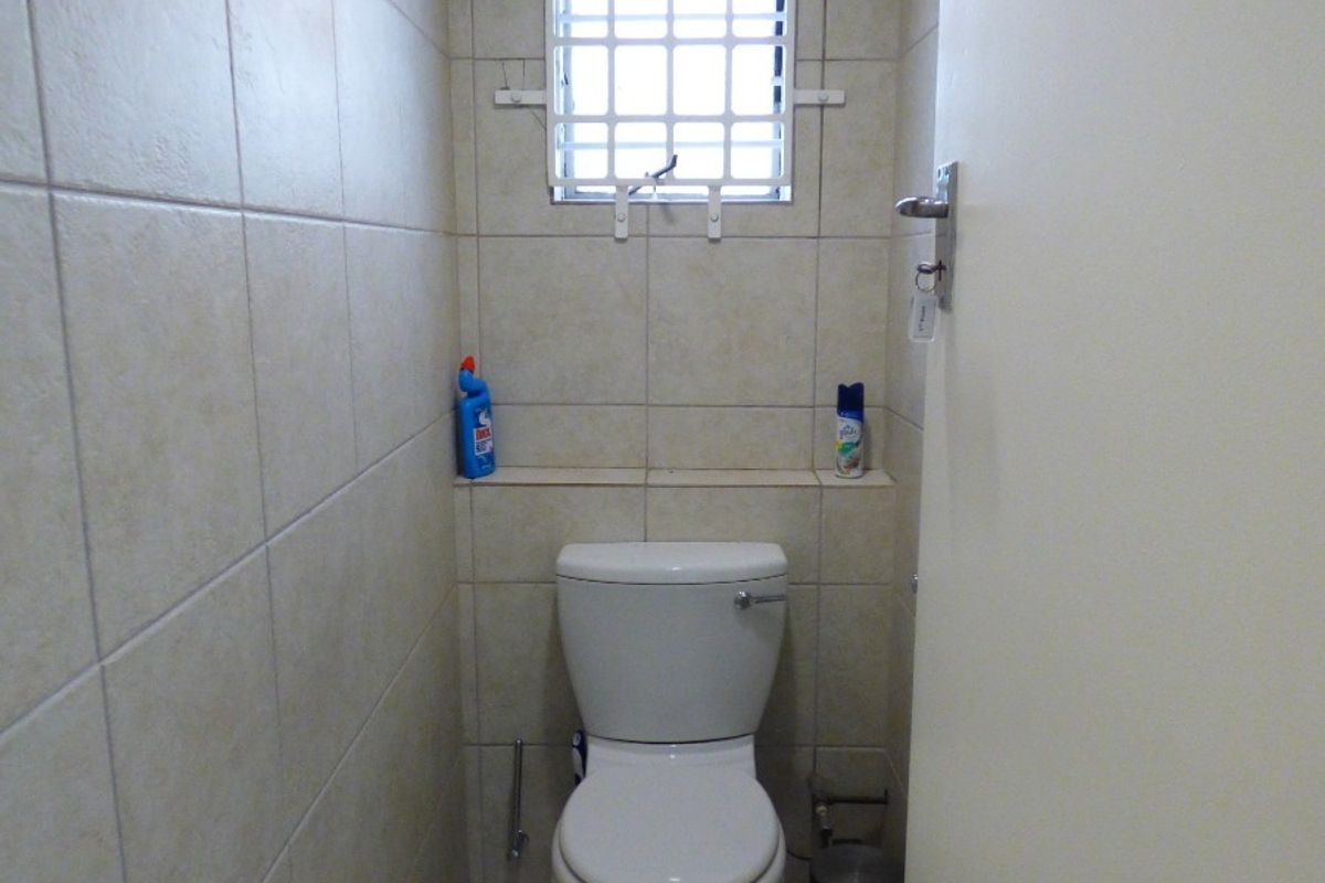 A compact guest bathroom featuring neutral ceramic wall and floor tiles, a standard toilet, and a small window with security bars.