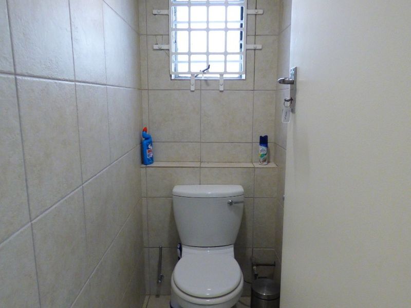 A compact guest bathroom featuring neutral ceramic wall and floor tiles, a standard toilet, and a small window with security bars.