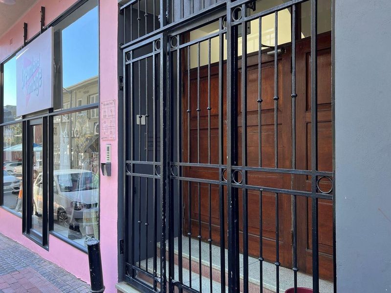 Commercial storefront entrance featuring a secure metal gate, solid timber double doors, and large display windows along a paved street frontage.
