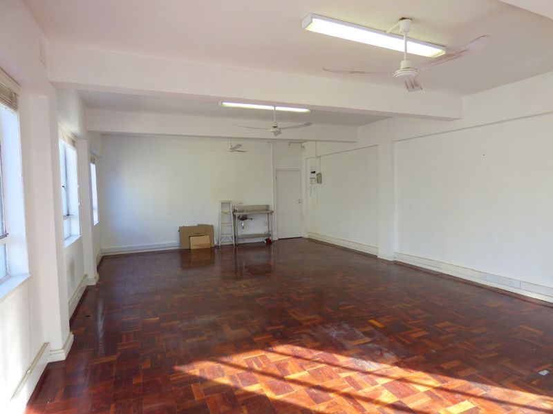Spacious open-plan office area featuring parquet flooring, ceiling fans, fluorescent lighting, and a small integrated stainless steel sink unit.