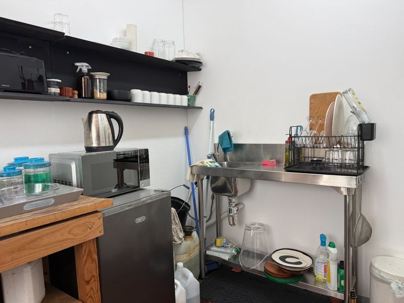 A functional scullery or utility prep area featuring a stainless steel sink, wall-mounted shelving, and integrated microwave space.