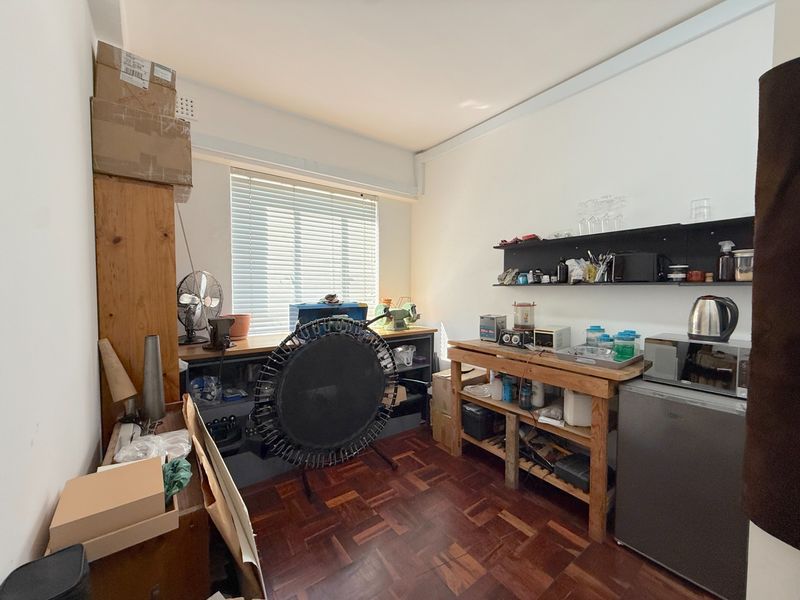 A functional utility or workspace featuring parquet flooring, wall-mounted shelving, and a window with venetian blinds, suitable for various commercial or storage purposes.
