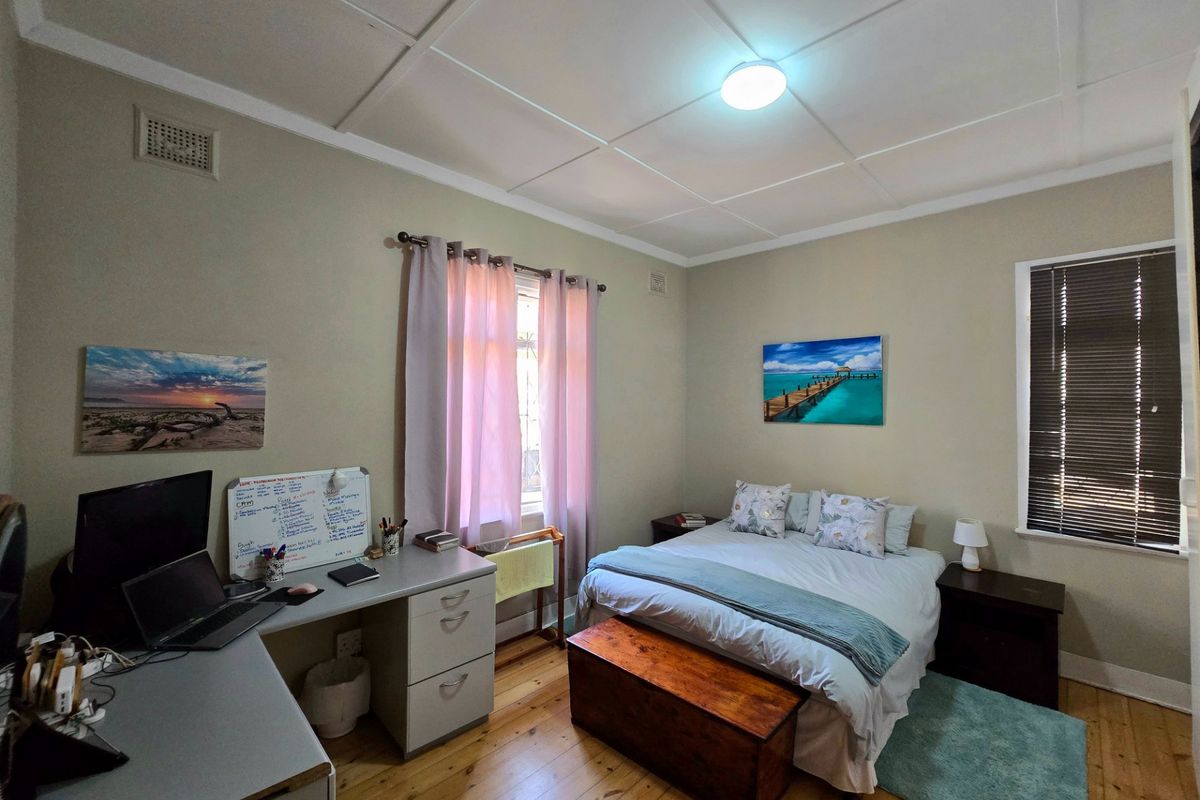 A functional bedroom featuring timber flooring and a tiled ceiling, offering a comfortable space with natural light from dual windows.