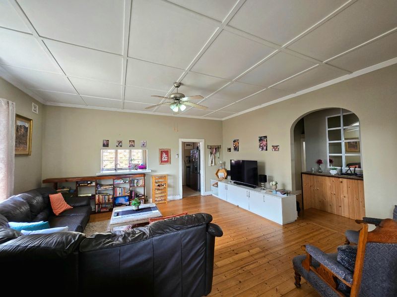Spacious living room featuring polished hardwood flooring, a distinctive coffered ceiling with a central fan, and an elegant arched entryway leading to adjacent spaces.
